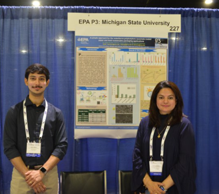 Two student researchers stand before a poster, sharing their findings at an academic event